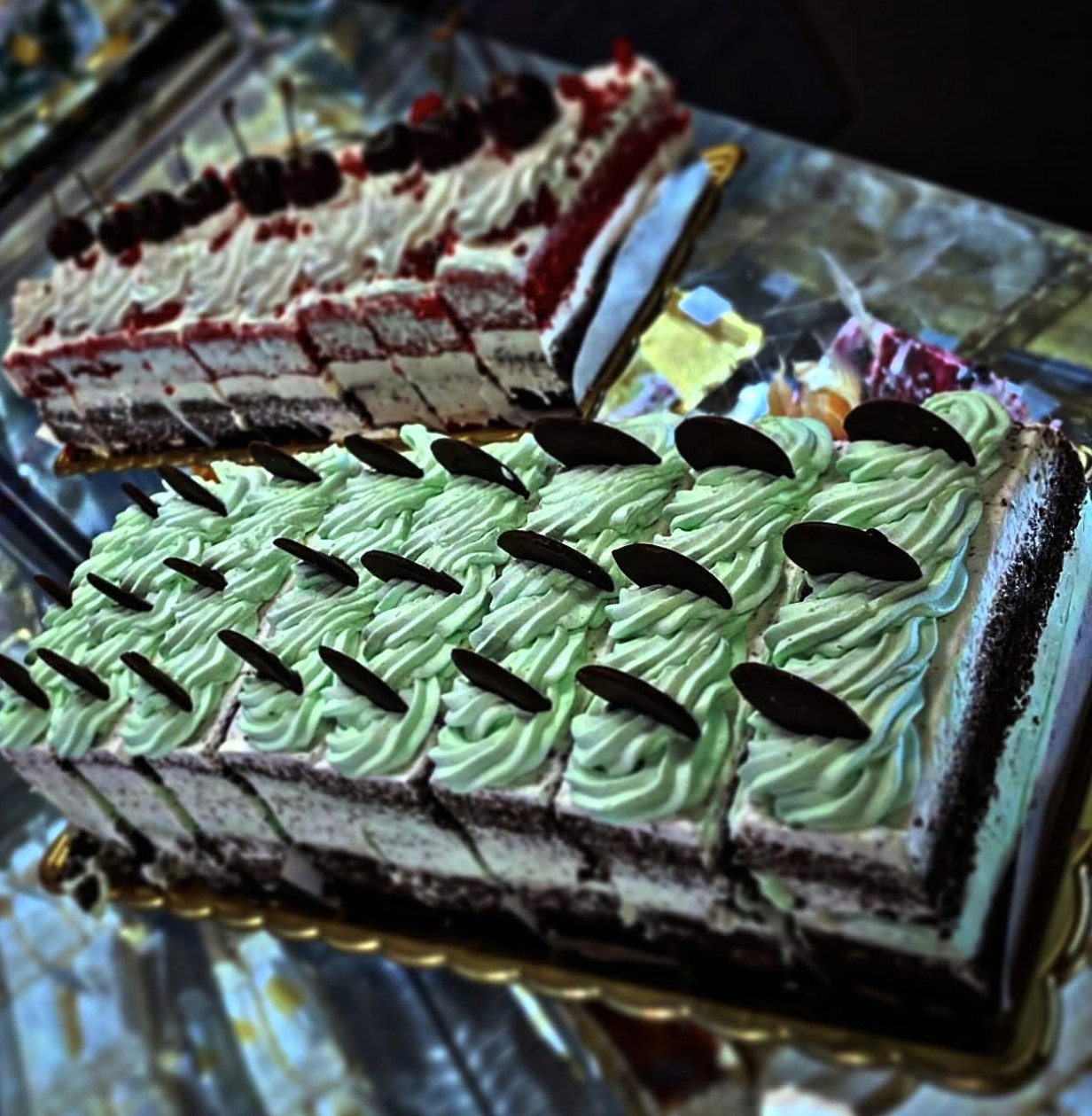 Bolos especiais já fatiados na montra, um com creme verde e lascas de chocolate